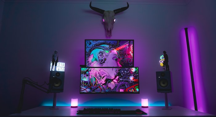 A desk with monitors and studio speakers in neon light